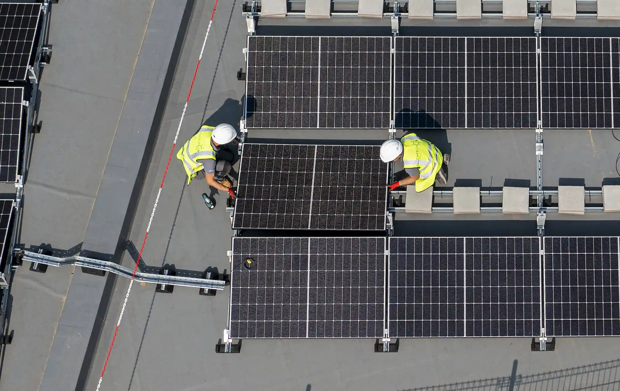 Two Utilita Business engineers carrying a commercial solar panel on top of a public sector building rooftop.