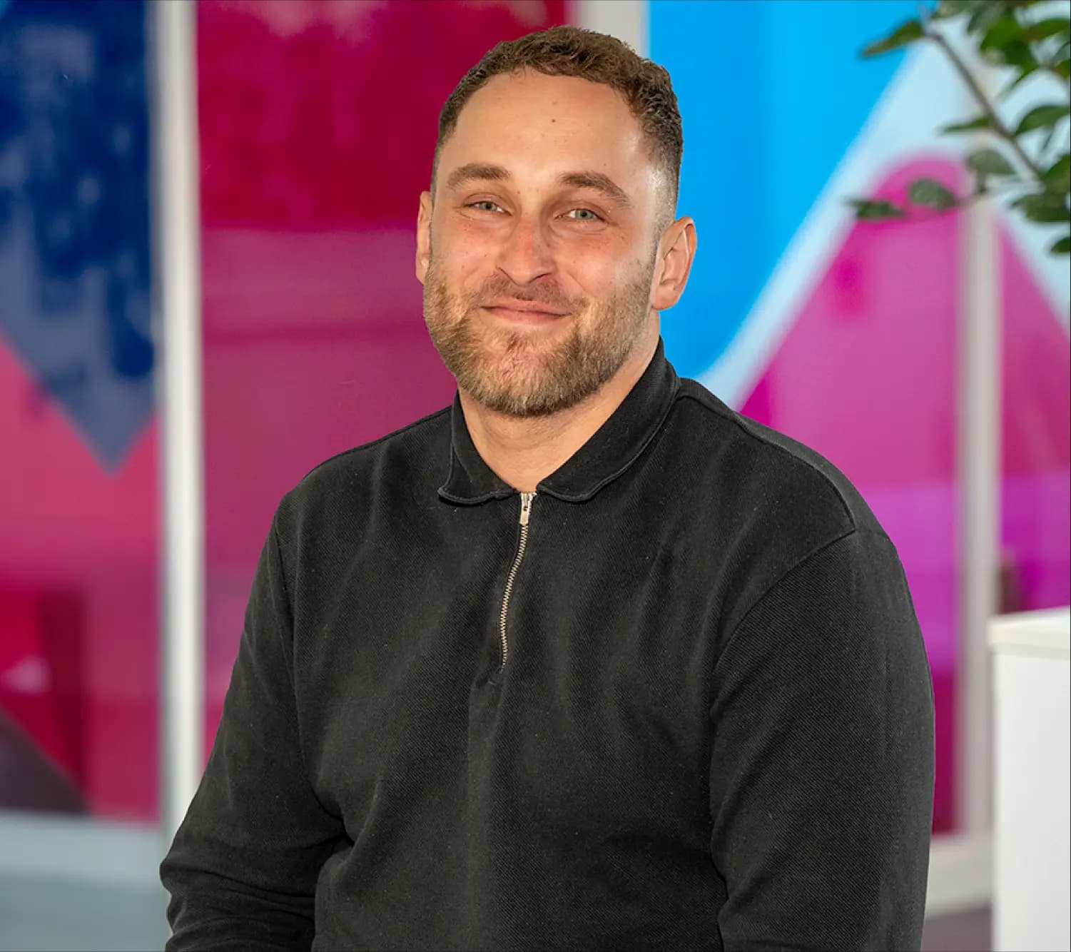 Photo of Arran Lord, Business Development Manager at Utilita Business, sat in front of colourful glass panels.